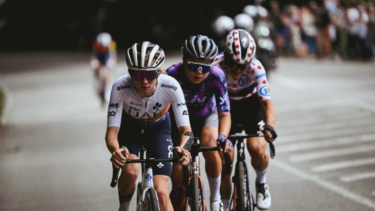 A group of cyclists racing together on an open road, riding in a tight pack during an outdoor cycling event.