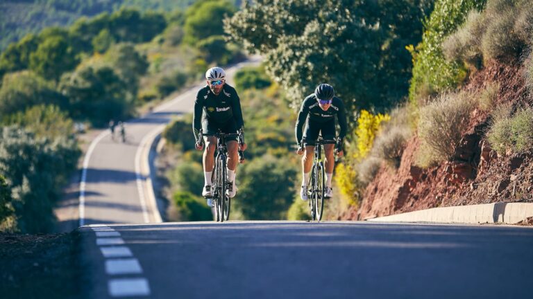 A fast-moving peloton of cyclists racing together on a road, demonstrating teamwork, speed, and endurance.