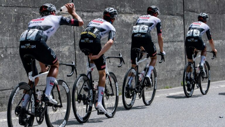 Group of cyclists racing with one athlete drinking water mid-ride to maintain hydration