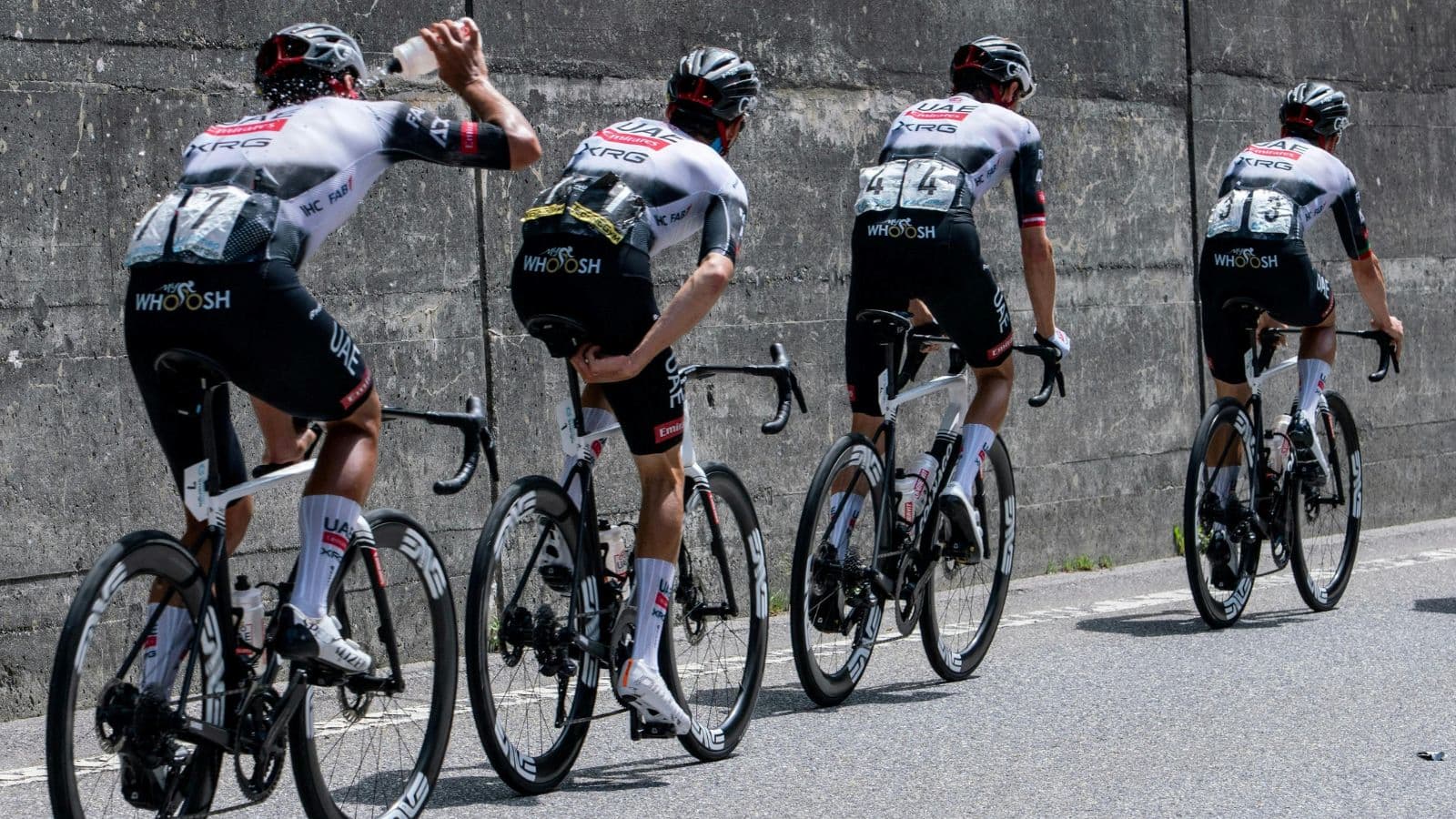 Group of cyclists racing with one athlete drinking water mid-ride to maintain hydration