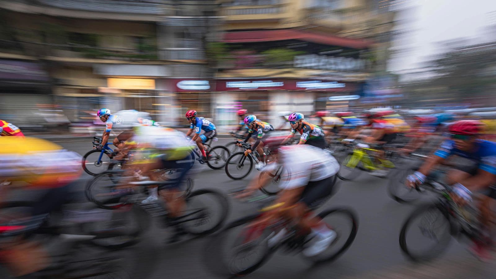 A group of cyclists racing at high speed in a competitive event, riding closely together on the road.