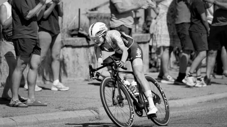 Bike fitter observing a cyclist’s foot, ankle, and knee alignment while the rider pedals on an indoor trainer.