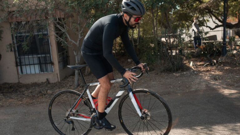 Road cyclist adjusting a fitted cycling jersey and bib short straps before riding to prevent rubbing and pressure from cycling clothing.